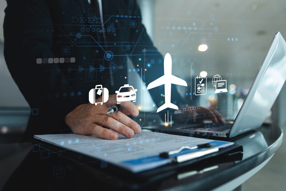 Eine Person im Anzug arbeitet an einem Laptop, darüber schweben digitale Symbole für Flugzeug, Koffer, Auto, Kalender und Computer vor einem dunklen Hintergrund.