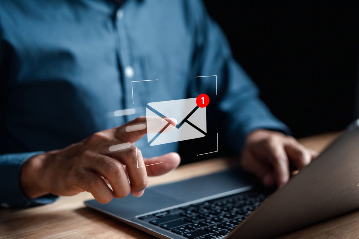 Eine Person in einem blauen Hemd tippt auf ein virtuelles E-Mail-Symbol mit einer roten Benachrichtigungsanzeige, das über einem Laptop auf dem Tisch schwebt.