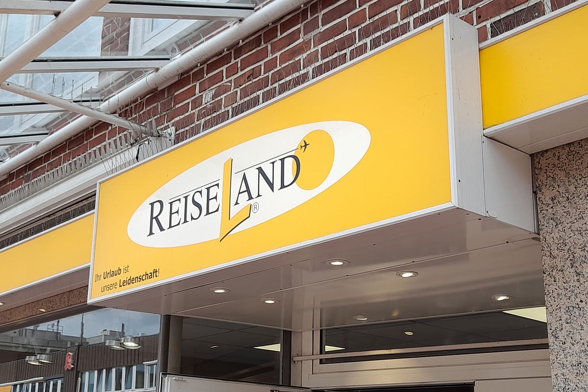 Schild von ReiseLand mit gelbem Hintergrund und schwarzer Schrift, das den Slogan 'Ihr Urlaub ist unsere Leidenschaft!' zeigt.