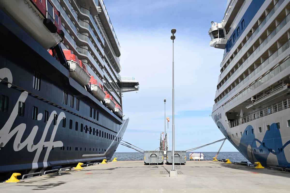 Zwei große Kreuzfahrtschiffe liegen nebeneinander an einem Hafen, mit Blick auf das Wasser und einem klaren Himmel.