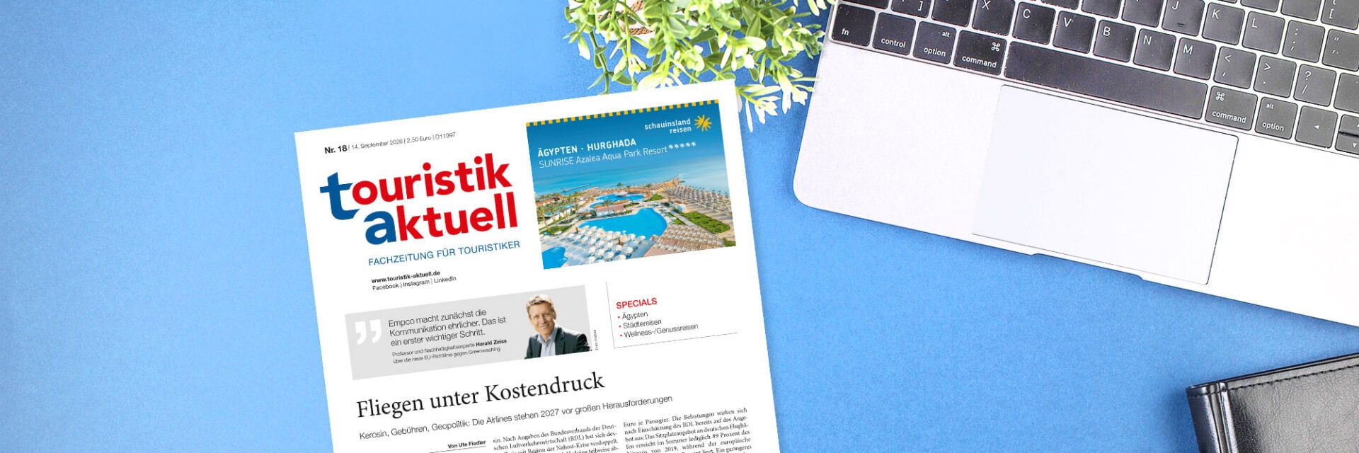 Die Titelseite der Fachzeitschrift touristik aktuell liegt neben einem Laptop und einer kleinen Pflanze auf einem hellblauen Untergrund auf einem Tisch.