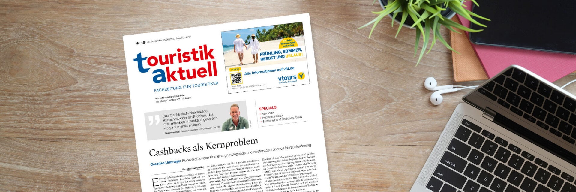 ta-header-19-26_BongkarnThanyakij Die Fachzeitschrift touristik aktuell liegt auf einem Holztisch neben einem Laptop, Kopfhörern und einer kleinen Pflanze in einem hellen Büroambiente.
