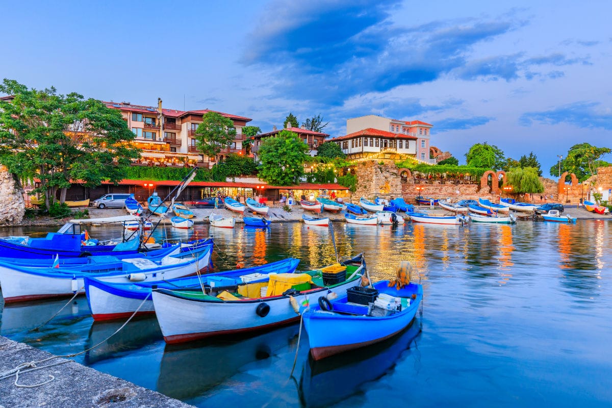 Blick auf den Hafen von Nessebar in Bulgarien bei Dämmerung mit zahlreichen kleinen Fischerbooten, die vor der historischen Küstenbebauung vor Anker liegen.