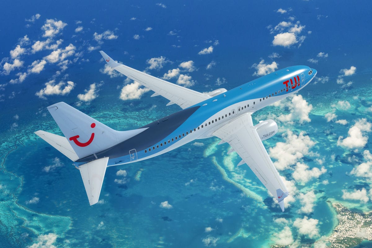 Ein blau-weißes Passagierflugzeug der Fluggesellschaft TUI fliegt in der Luft über einer tropischen Inselgruppe mit türkisfarbenem Meer und weißen Wolken.