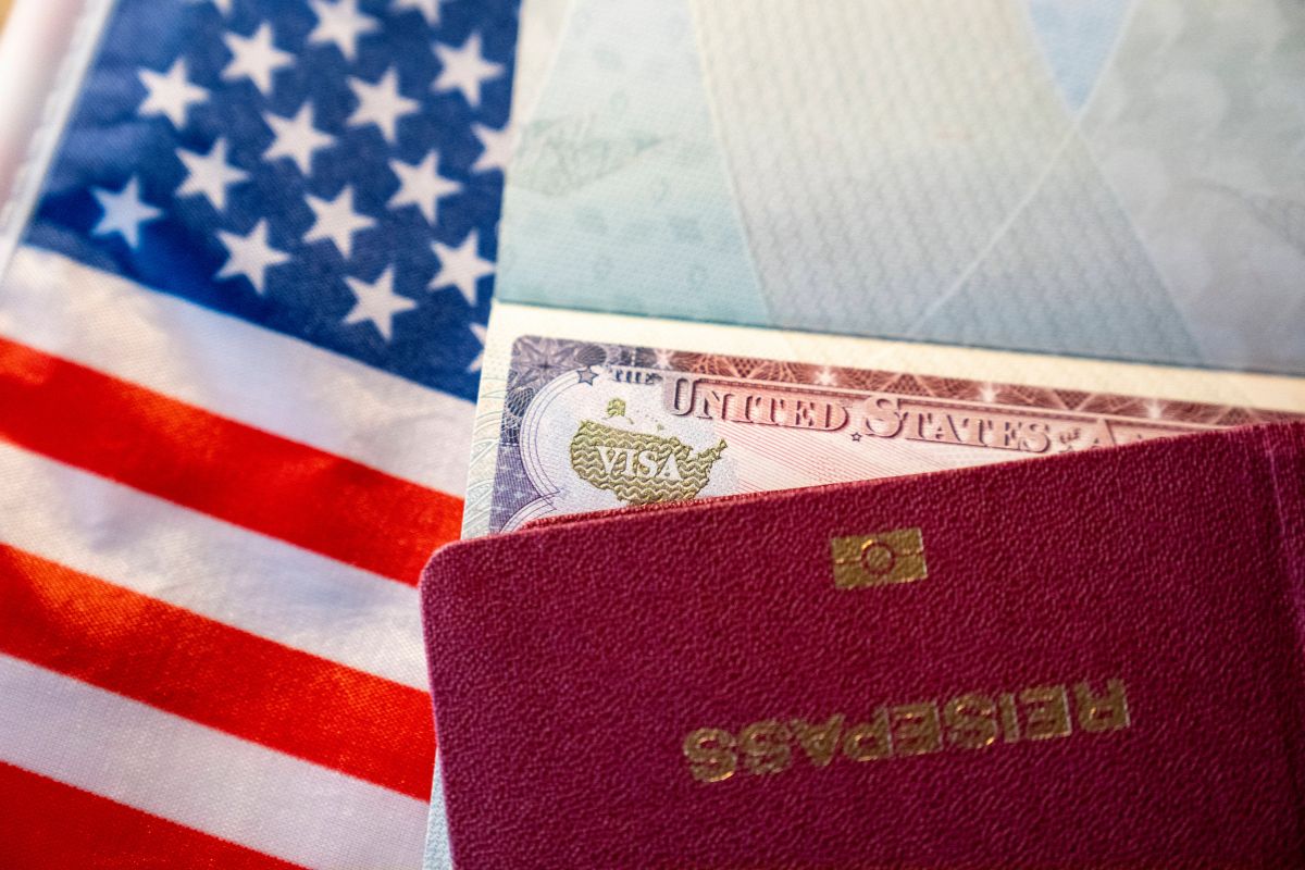 Ein aufgeklappter Reisepass mit einem eingeklebten Visum für die Vereinigten Staaten liegt auf einer ausgebreiteten Flagge der USA im Hintergrund.