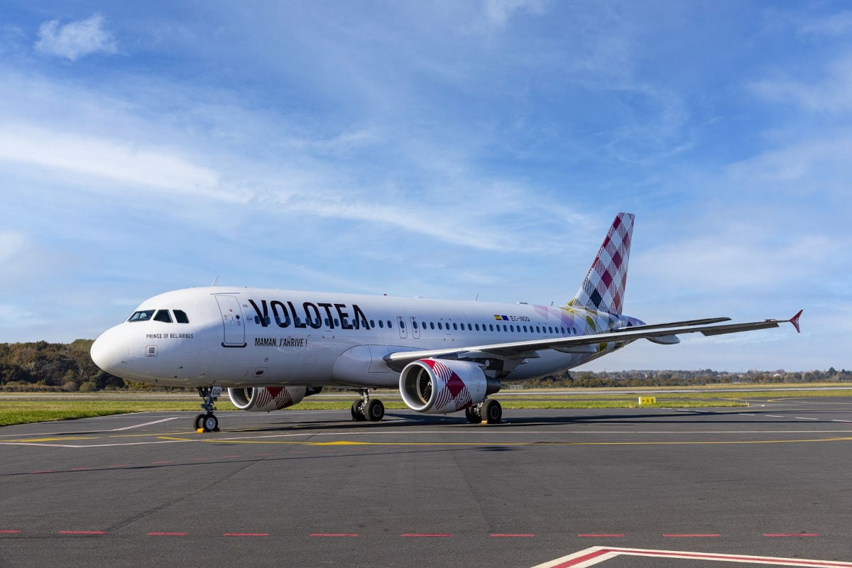 Ein weißes Passagierflugzeug der Fluggesellschaft Volotea steht auf einem Rollfeld vor einem blauen Himmel mit leichten Wolken am helllichten Tag.