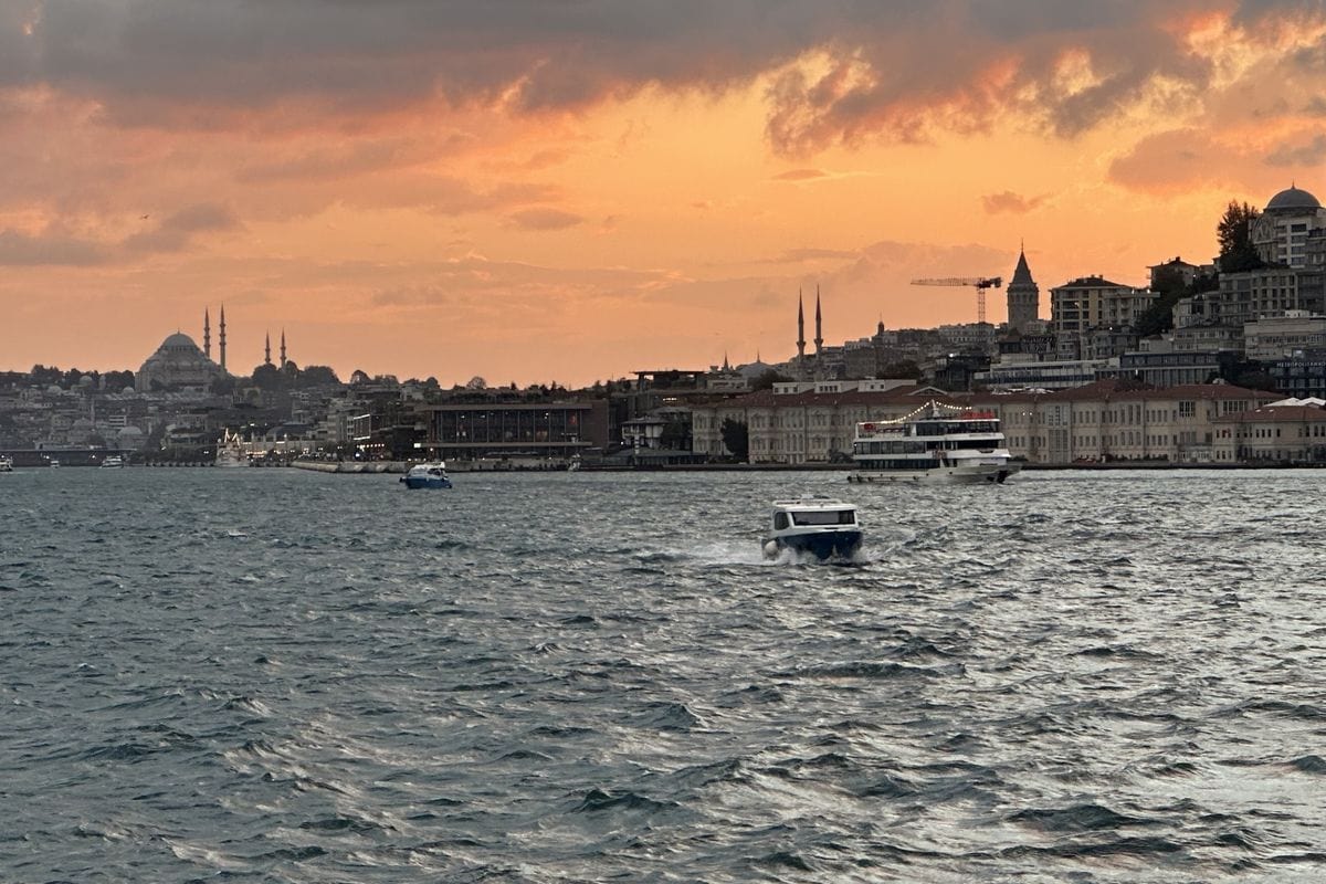 Blick auf den Bosporus in Istanbul bei Sonnenuntergang mit verschiedenen Booten auf dem Wasser und der Silhouette der Stadt mit Moscheen im Hintergrund.