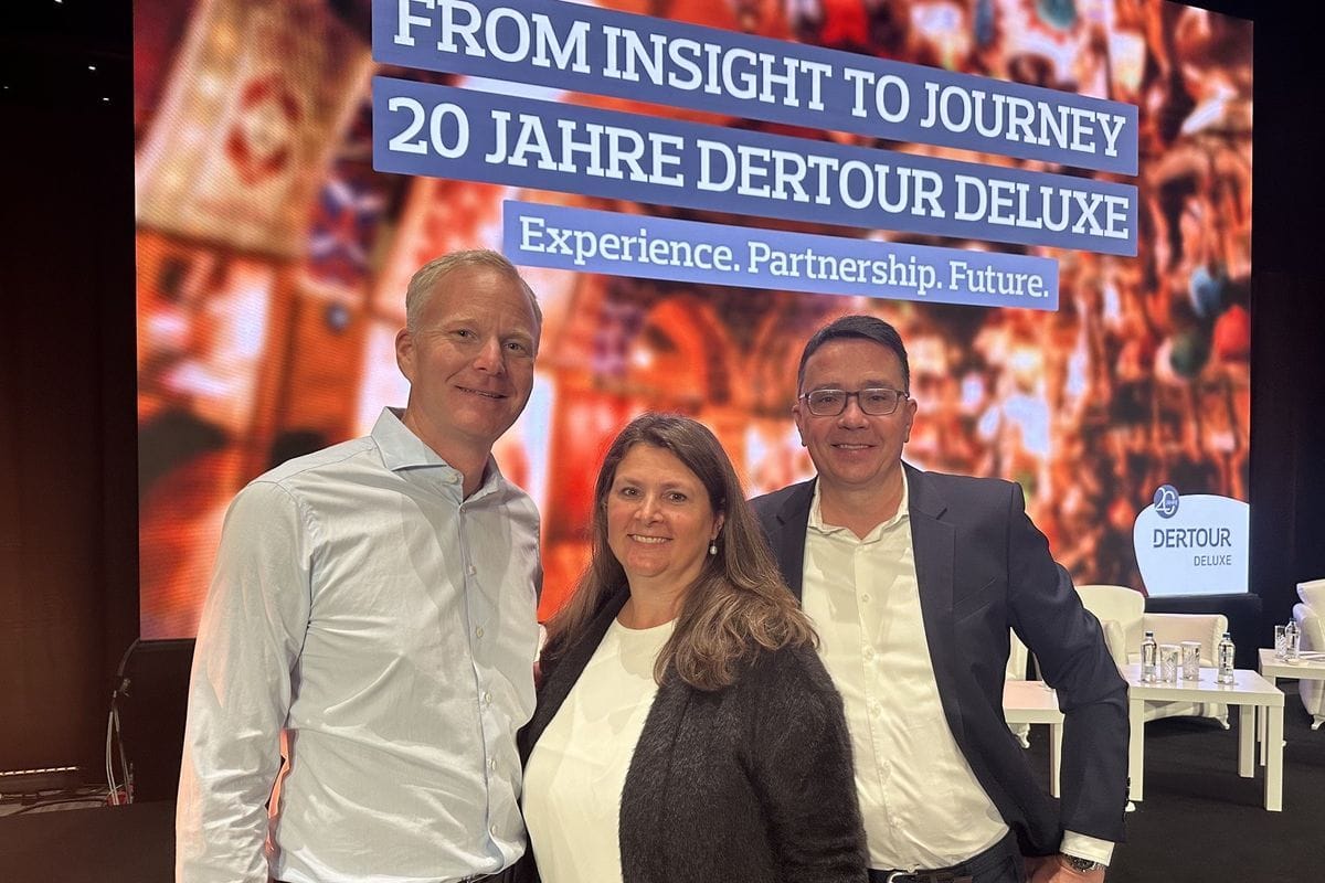 Drei Personen stehen nebeneinander vor einer großen Leinwand mit der Aufschrift 20 Jahre Dertour Deluxe und lächeln in die Kamera bei einer Veranstaltung.