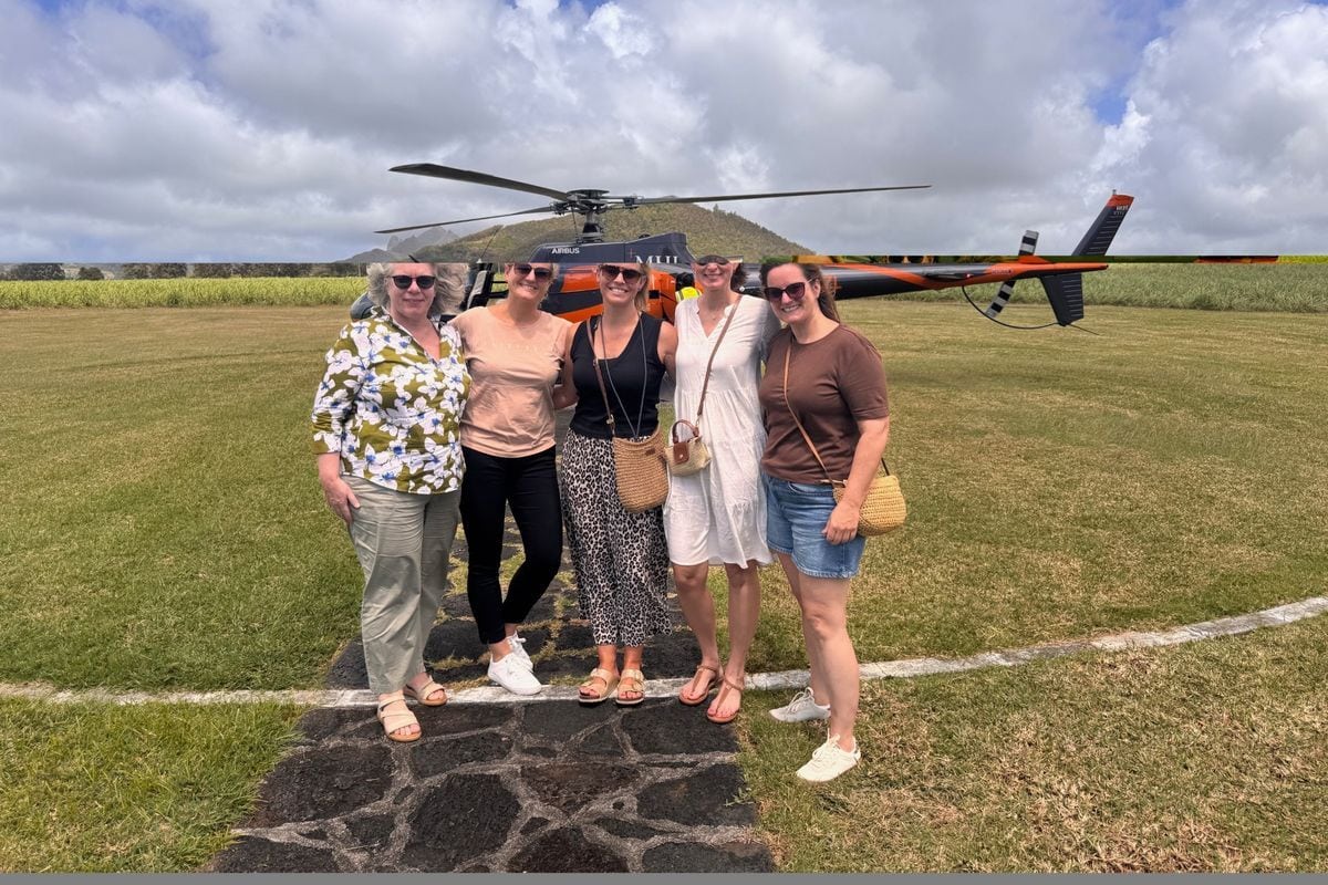 Fünf Frauen stehen nebeneinander auf einem gepflasterten Weg vor einem Airbus-Hubschrauber auf einer grünen Wiese unter einem bewölkten Himmel im Freien.