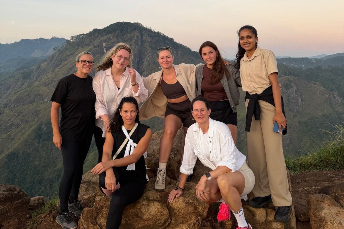 Eine Gruppe von sieben Frauen posiert gemeinsam auf einem Felsen vor einer bergigen Landschaft während der Dämmerung in entspannter, sommerlicher Kleidung.