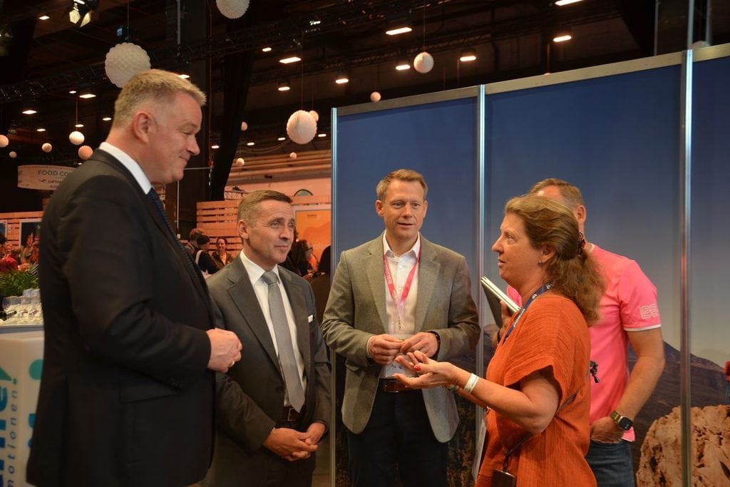 Eine Gruppe von vier Personen steht in einer Messehalle zusammen und führt ein Gespräch. Zwei Männer tragen Anzüge, ein Mann ein Sakko, eine Frau ein Oberteil.