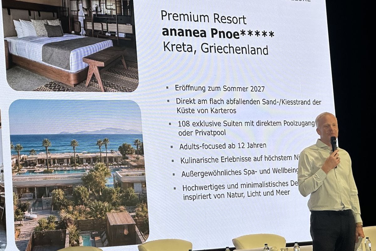 Ein Mann steht vor einer großen Leinwand, die ein Hotelzimmer, eine Außenansicht eines Resorts am Meer und eine Liste mit Textinformationen präsentiert.