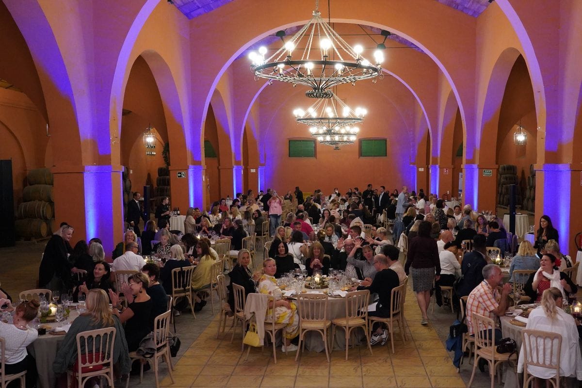 Ein großer, gewölbter Saal mit orangefarbenen Wänden, violetten Lichtakzenten und mehreren Kronleuchtern, in dem zahlreiche Gäste an runden Tischen sitzen.