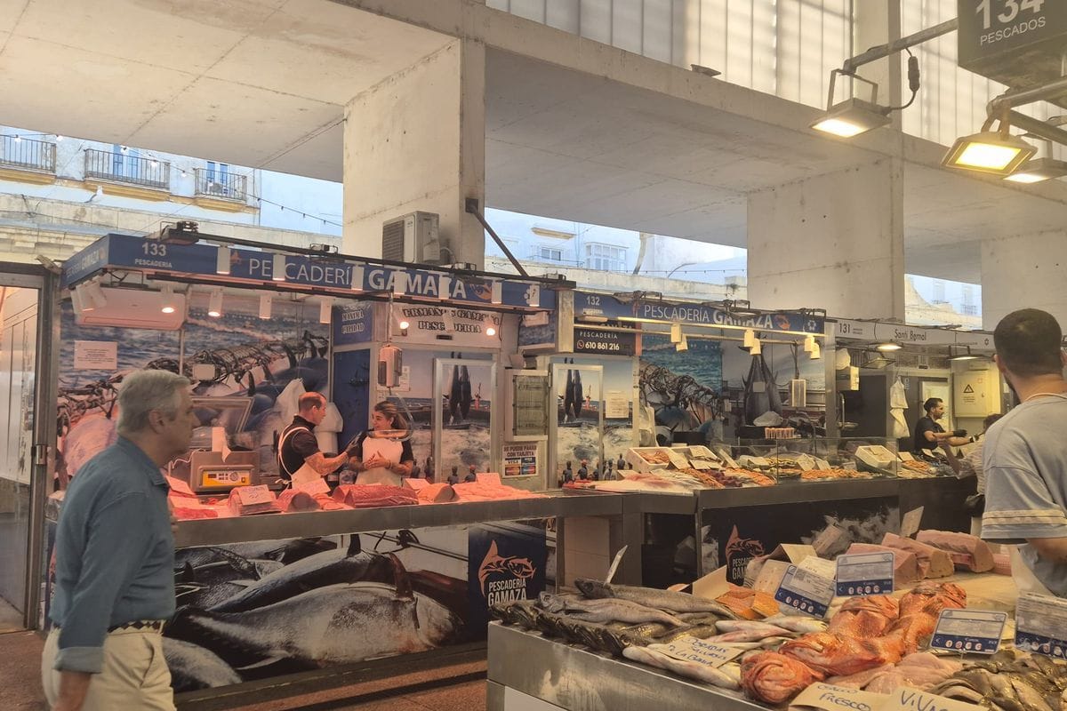 Ein Fischmarkt mit mehreren Verkaufsständen, an denen frischer Fisch und Meeresfrüchte auf Eis präsentiert werden, während Kunden an den Theken stehen.