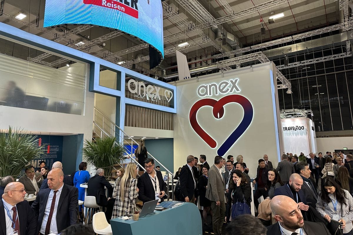Blick auf einen belebten Messestand mit dem großen Firmenlogo von anex in Herzform an einer weißen Wand und zahlreichen Personen in geschäftlicher Kleidung.