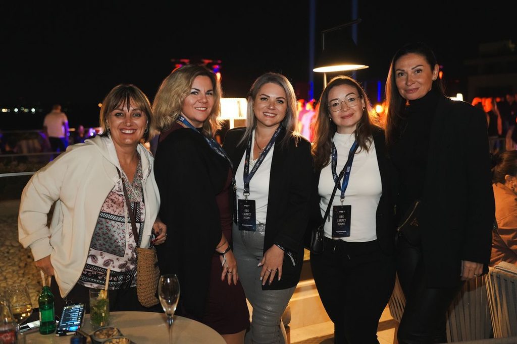 Fünf Frauen stehen abends nebeneinander auf einer Terrasse und lächeln in die Kamera. Sie tragen Namensschilder an Schlüsselbändern um den Hals.