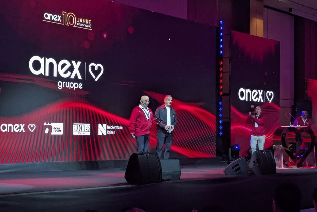 Zwei Männer stehen auf einer Bühne vor einer großen LED-Wand mit dem Logo der Anex Gruppe und weiteren Markenlogos bei einer Firmenveranstaltung.