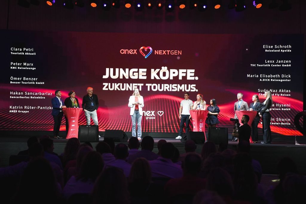 Eine Gruppe von Menschen steht auf einer Bühne vor einem großen Bildschirm mit dem Text Junge Köpfe. Zukunft Tourismus. und Namen von Teilnehmern.