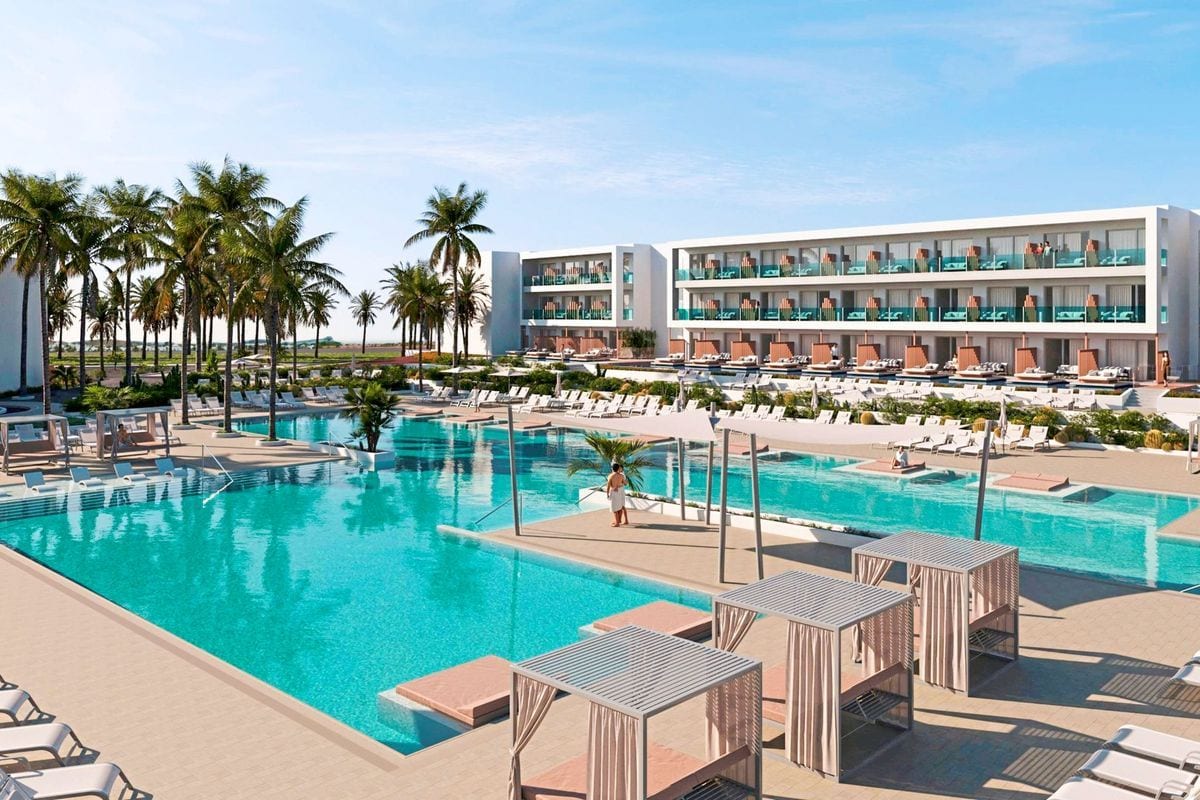 Eine weitläufige Hotelanlage mit einem großen, türkisfarbenen Pool, umgeben von Palmen, zahlreichen Sonnenliegen und modernen, überdachten Lounge-Bereichen.