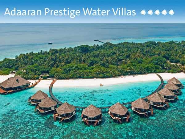 Luftaufnahme der Adaaran Prestige Water Villas mit kreisförmig angeordneten Stelzenhäusern über türkisfarbenem Wasser vor einer tropischen Insel mit Palmen.