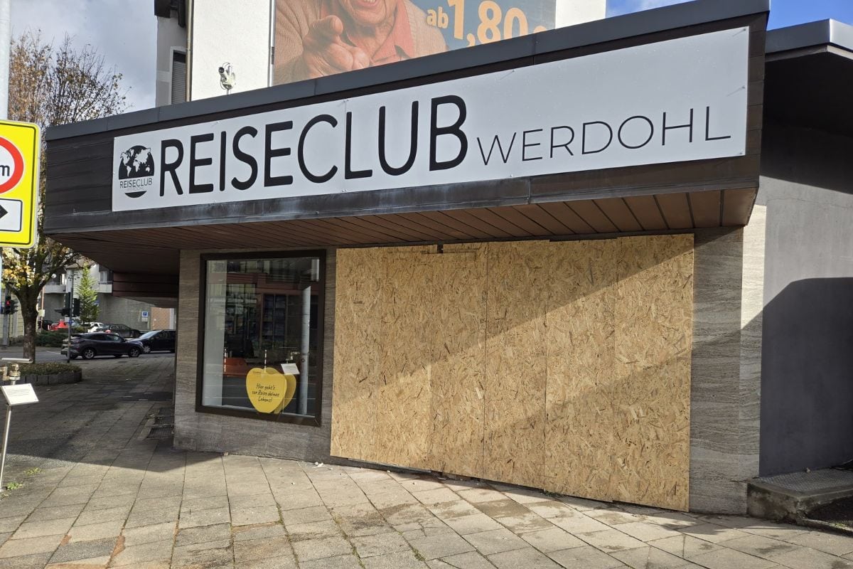 Die Außenansicht des Reiseclub Werdohl mit einem großen Firmenschild über dem Eingang, dessen Schaufensterfront teilweise mit OSB-Holzplatten verdeckt ist.