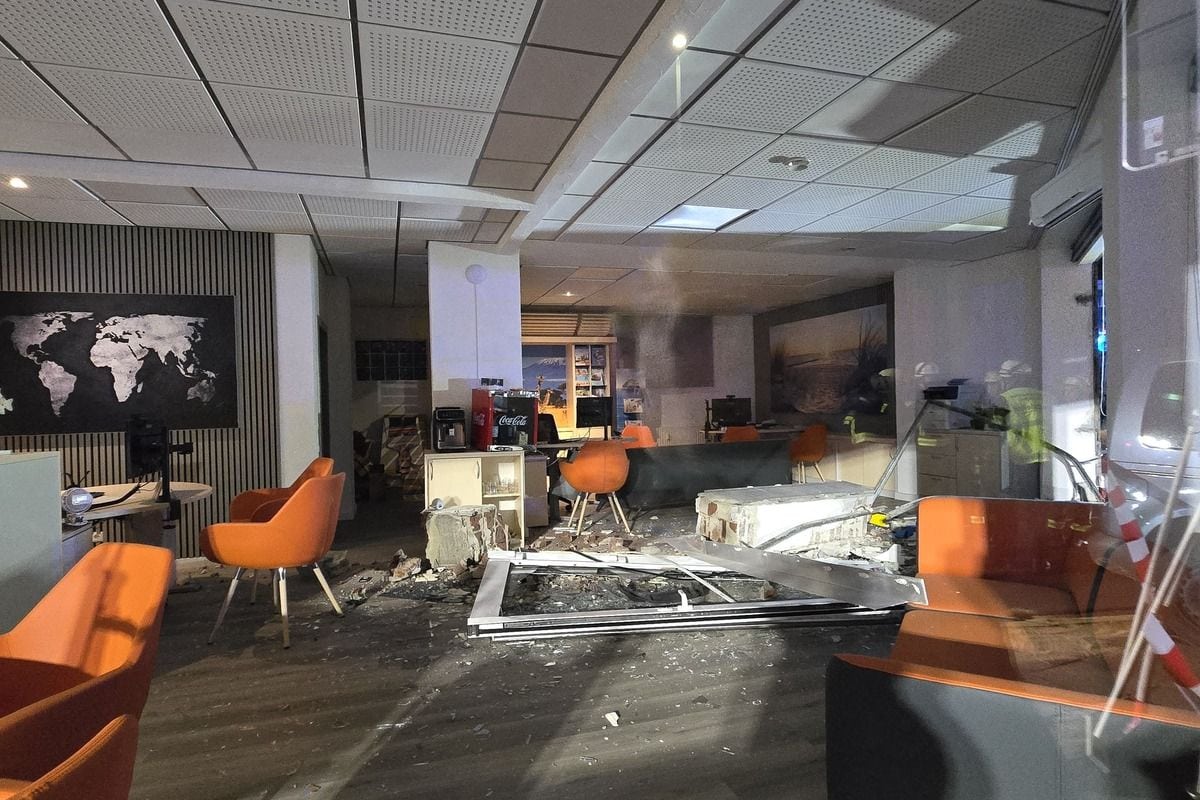 Ein verwüstetes Büro mit zerstörter Glasfront, Trümmern auf dem Boden, umgestürzten Möbeln und orangefarbenen Sesseln in einem modernen Innenraum.