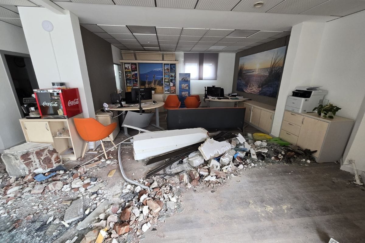 Ein verwüstetes Büro mit einem großen Trümmerhaufen aus Mauerwerk und Schutt auf dem Boden, umgeben von Büromöbeln, Stühlen und technischer Ausstattung.