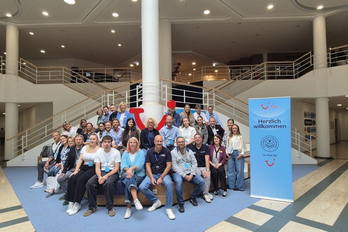 Eine große Gruppe von Menschen posiert für ein Foto in einer hellen Hotelhalle vor einer Treppe mit einem TUI-Logo und einem Willkommens-Roll-up-Banner.