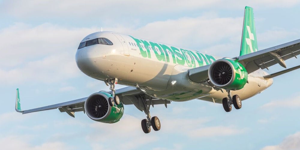 Ein Passagierflugzeug der Fluggesellschaft Transavia im Landeanflug mit ausgefahrenem Fahrwerk vor einem hellblauen Himmel mit leichten Wolkenschleiern.