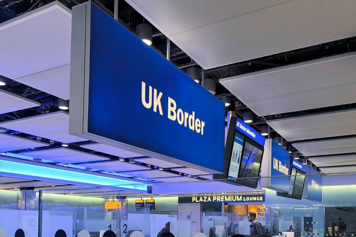 Ein großes, blaues Schild mit der gelben Aufschrift UK Border hängt an der Decke eines Flughafenterminals über den Schaltern der Grenzkontrolle.