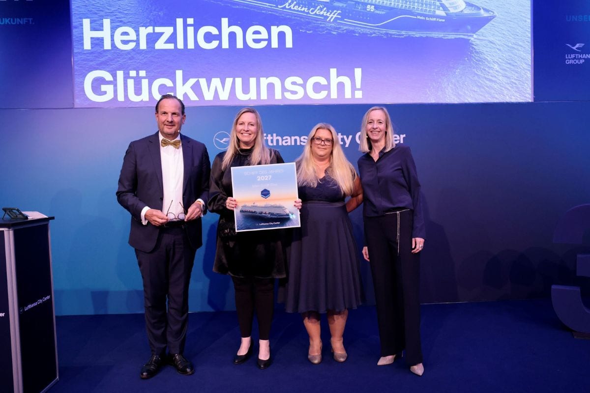 Vier Personen stehen auf einer Bühne vor einer Leinwand mit der Aufschrift Herzlichen Glückwunsch und halten gemeinsam eine gerahmte Auszeichnung in Händen.