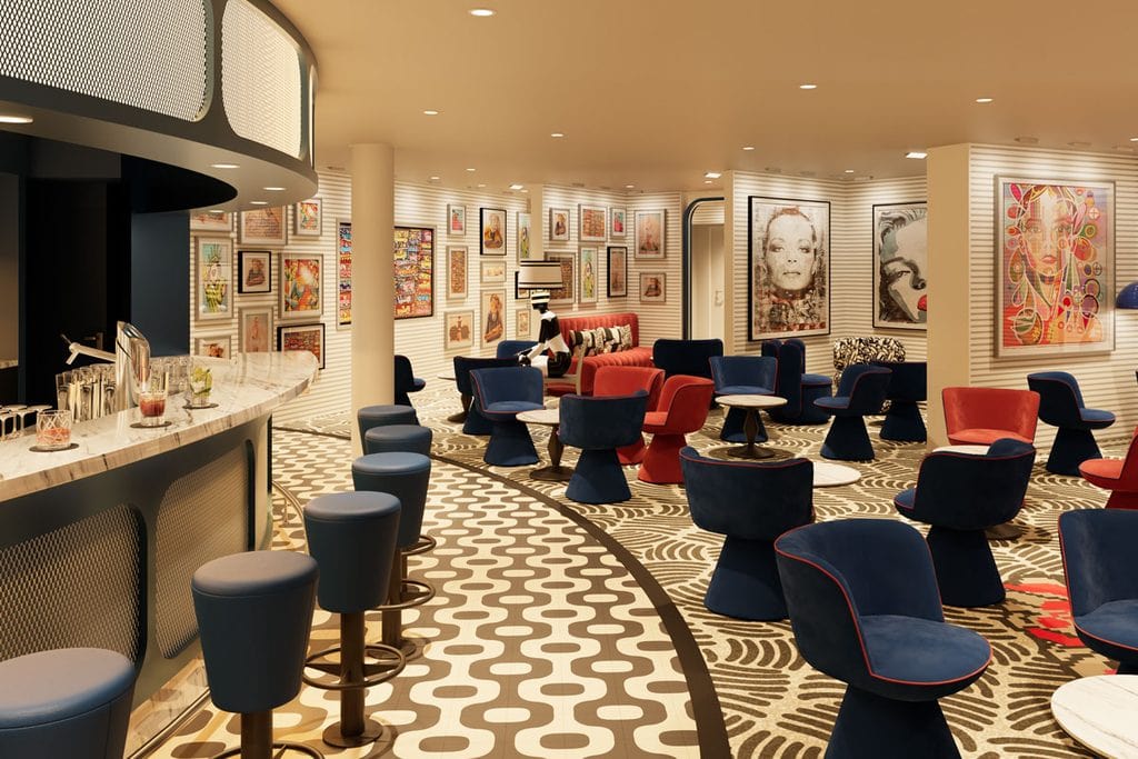 Innenansicht einer Bar mit geschwungener Theke, blauen Barhockern, roten und blauen Sesseln sowie zahlreichen gerahmten Kunstwerken an den hellen Wänden.