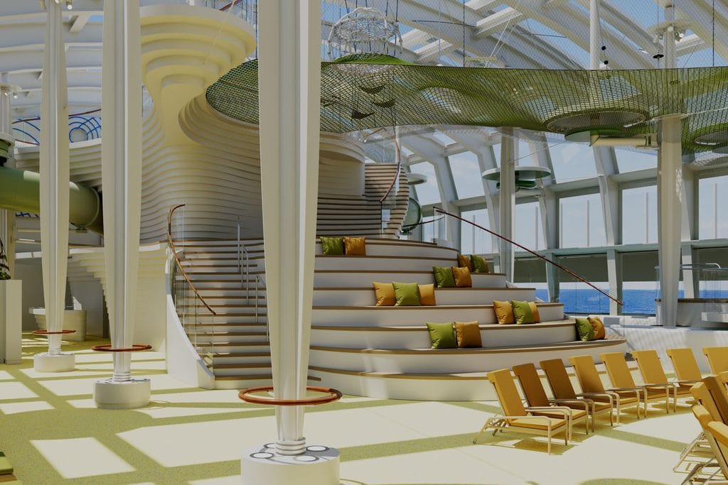 Ein heller Innenbereich mit einer geschwungenen Treppe, Sitzstufen mit grünen und gelben Kissen, hohen Säulen und einem grünen Netz unter einer Glasdecke.