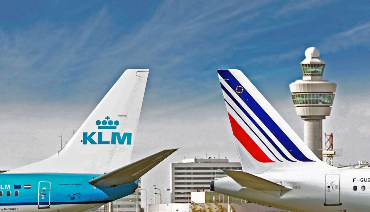 Die Seitenleitwerke zweier Flugzeuge der Airlines KLM und Air France stehen nebeneinander vor einem Kontrollturm auf einem Flughafen bei blauem Himmel.