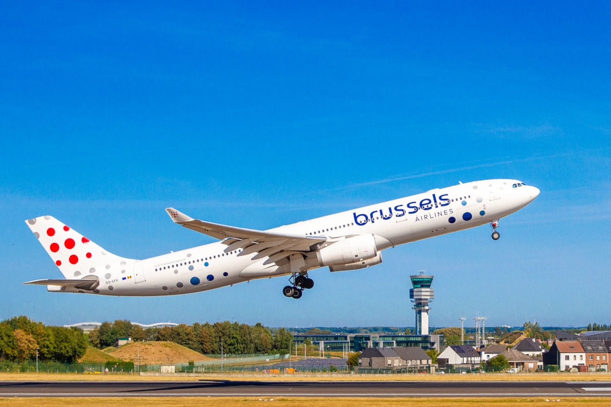 Ein Passagierflugzeug der Brussels Airlines mit markantem Punktemuster am Heck startet bei strahlend blauem Himmel von einer Startbahn vor einem Kontrollturm.