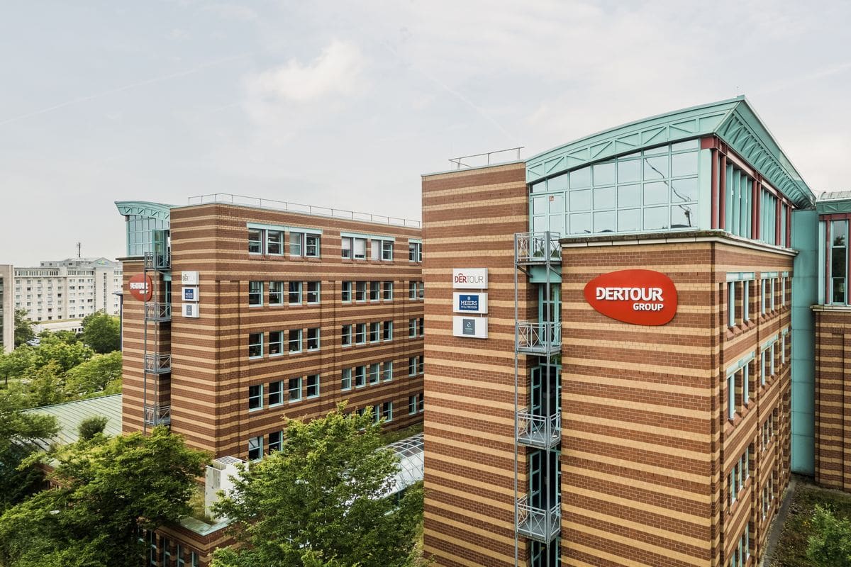 Die Außenansicht eines modernen Bürogebäudes mit gestreifter Klinkerfassade und dem roten Logo der Dertour Group an der Ecke unter einem bewölkten Himmel.