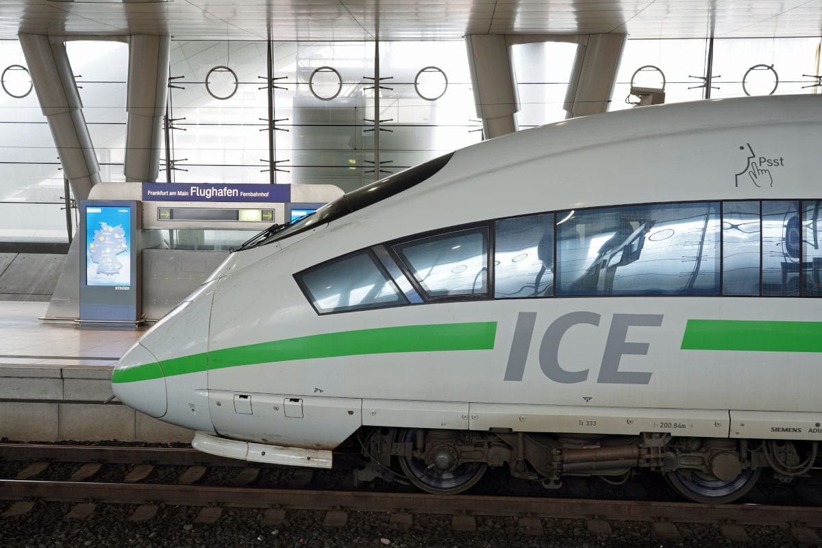 Die Seitenansicht eines ICE-Zuges mit grünem Streifen steht am Bahnhof Frankfurt am Main Flughafen Fernbahnhof unter einer modernen Glas-Stahl-Konstruktion.