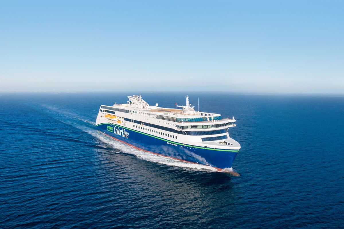 Die Color Hybrid von Color Line fährt auf dem tiefblauen Meer unter einem klaren Himmel. Das Passagierschiff ist von schräg oben in der Totalen zu sehen.