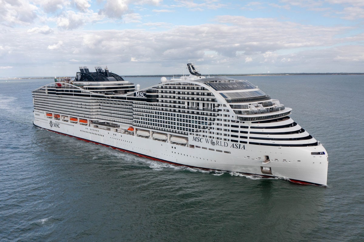 Das Kreuzfahrtschiff MSC World Asia fährt auf dem offenen Meer unter einem bewölkten Himmel. Die Seitenansicht zeigt das weiße Schiff mit vielen Decks.