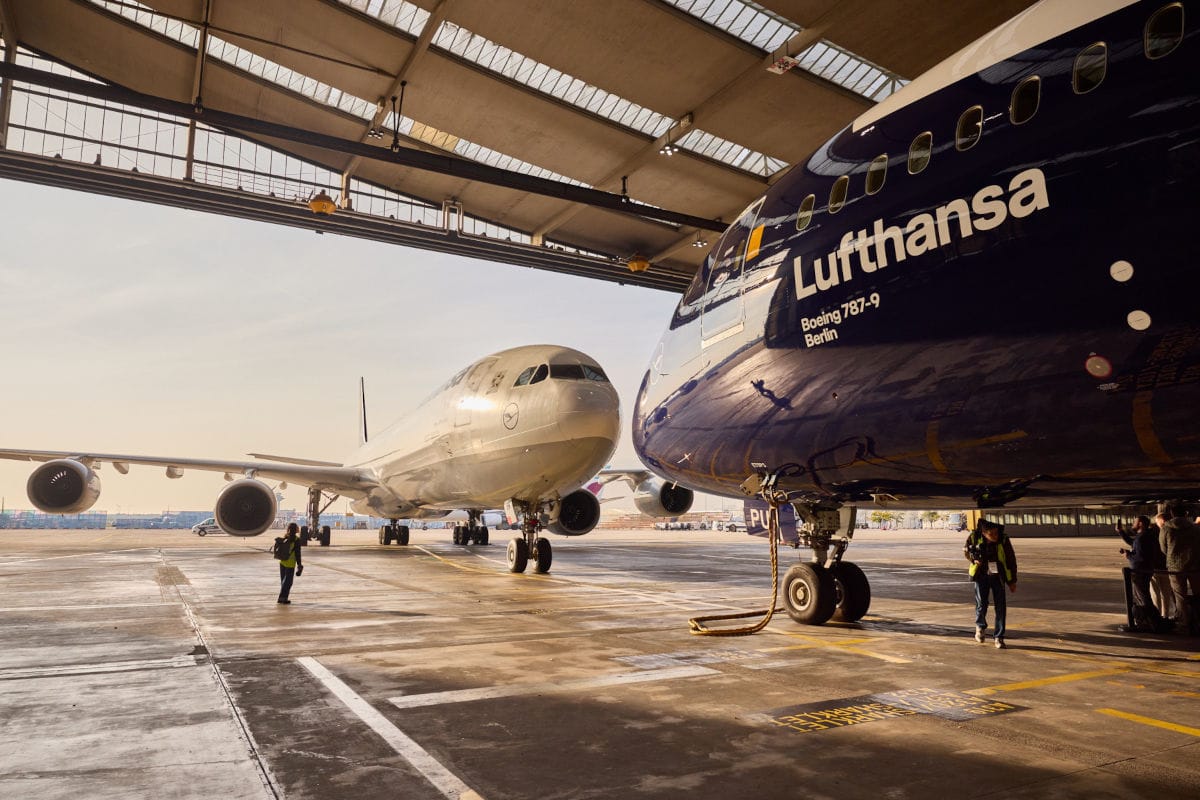 Zwei Flugzeuge stehen in einer großen Flugzeughalle. Rechts ist der vordere Teil einer dunkelblauen Boeing 787-9 der Lufthansa mit Schriftzug zu sehen.