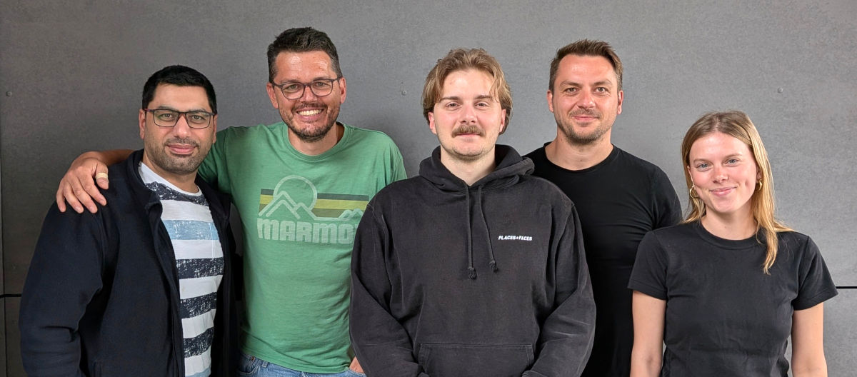 mile-mio-spezialveranstalter-ki Eine Gruppe von fünf Personen steht nebeneinander vor einer grauen Wand. Die drei Männer und zwei Frauen lächeln freundlich in die Kamera des Fotografen.