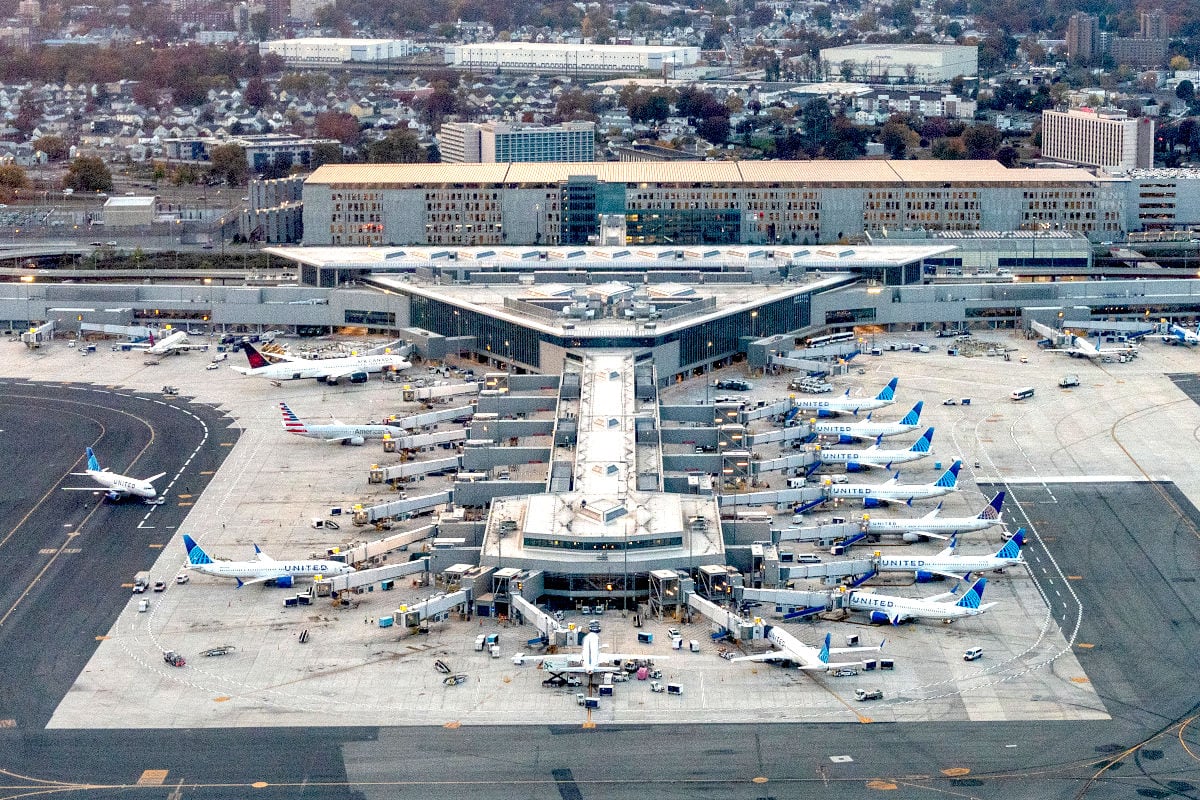 Luftaufnahme eines großen Flughafenterminals mit zahlreichen angedockten Flugzeugen verschiedener Fluggesellschaften auf dem weitläufigen Vorfeld.