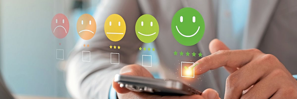 reisebuero-traveltech-umfrage Eine Person tippt auf einem Smartphone, während darüber eine Skala mit fünf farbigen Smileys und Auswahlkästchen für eine digitale Bewertung eingeblendet ist.