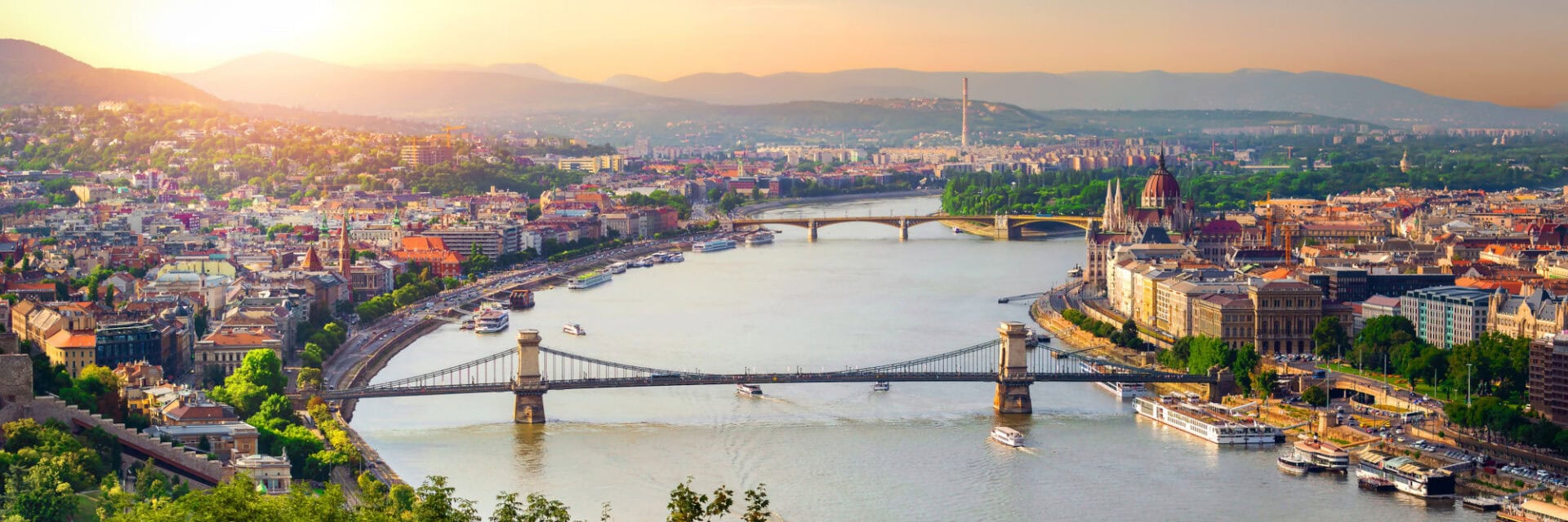 Panoramablick auf Budapest bei Sonnenuntergang mit der Kettenbrücke über der Donau, dem ungarischen Parlamentsgebäude und der Stadtkulisse im Hintergrund.