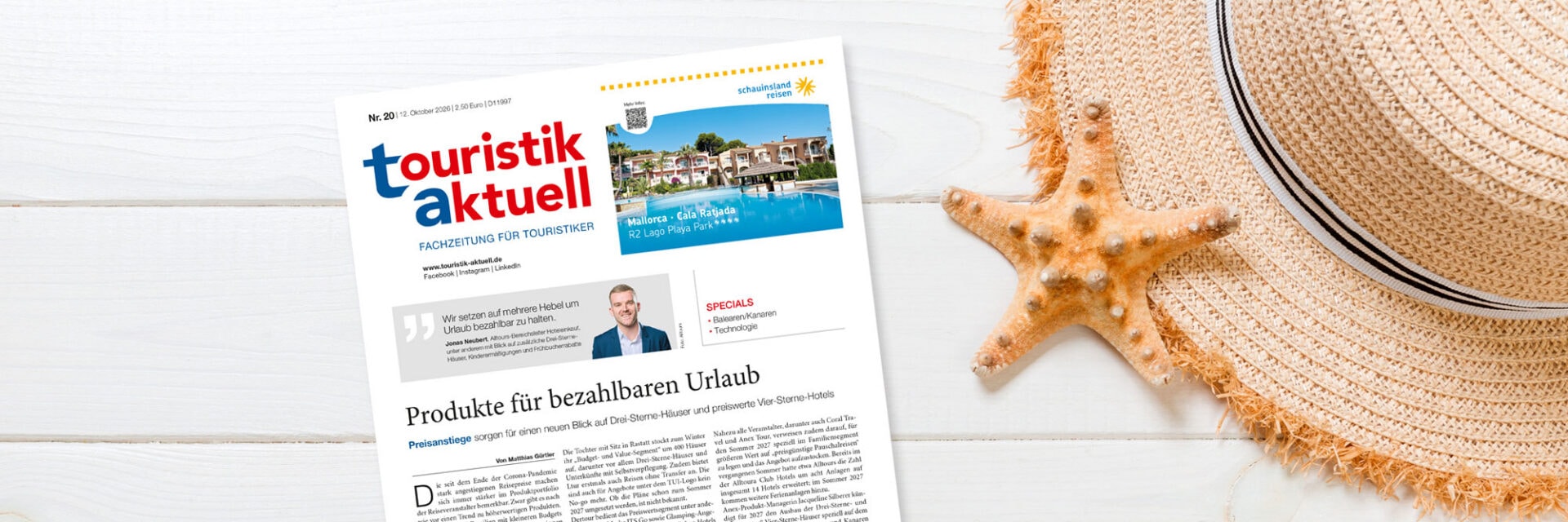 ta-header-20-26_Mykola-Sosiukin Die Titelseite der Fachzeitung touristik aktuell liegt auf einem weißen Holztisch neben einem beigen Strohhut und einem hellbraunen Seestern aus Kalk.