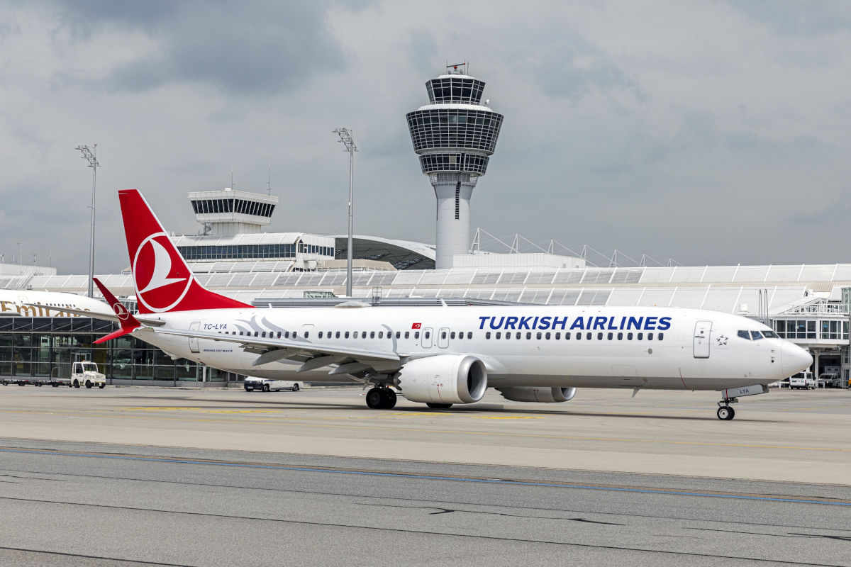 Ein Passagierflugzeug der Turkish Airlines rollt auf dem Rollfeld eines Flughafens vor einem markanten Kontrollturm unter einem bewölkten Himmel vorbei.