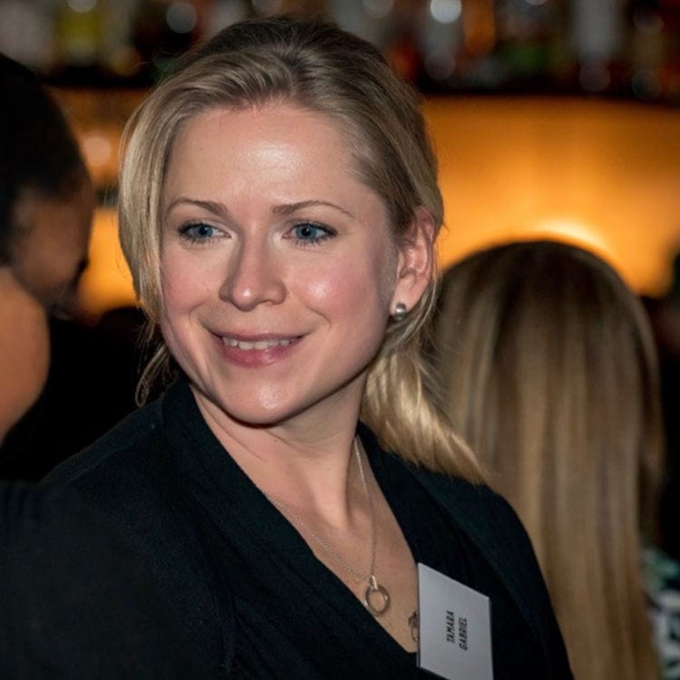 Eine blonde Frau mit blauem Blick lächelt leicht in die Kamera. Sie trägt ein schwarzes Oberteil, eine Halskette und ein Namensschild mit Tamara Gabriel.