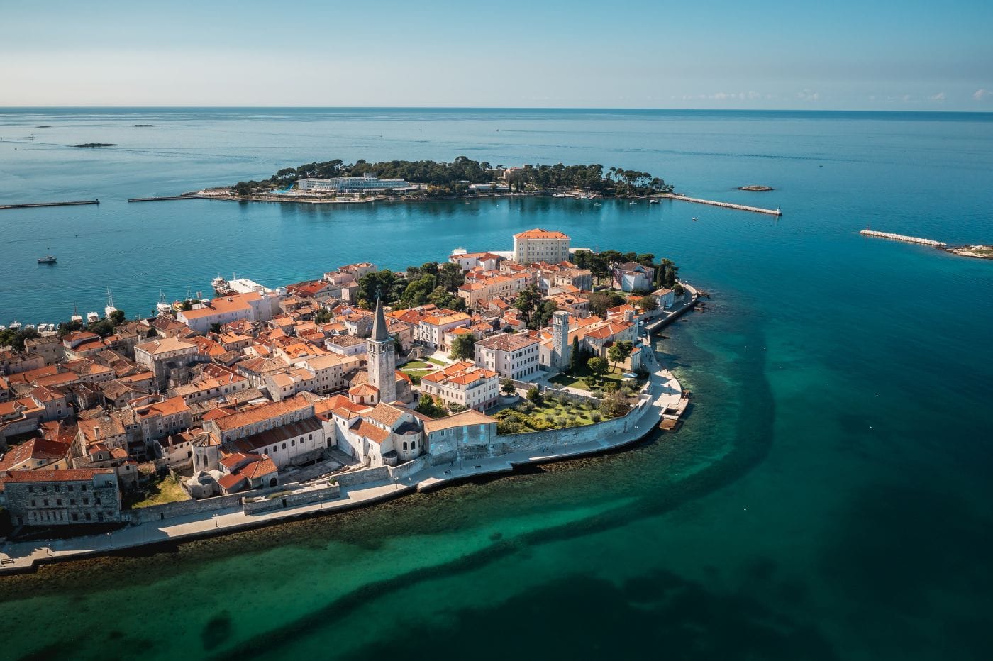 Luftaufnahme der historischen Altstadt von Poreč auf einer Halbinsel in Kroatien, umgeben von blauem Meer mit einer vorgelagerten Insel im Hintergrund.