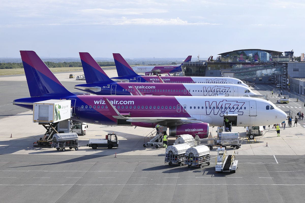 Mehrere Flugzeuge der Fluggesellschaft Wizz Air stehen auf dem Rollfeld eines Flughafens an ihren Parkpositionen, umgeben von Bodenabfertigungsfahrzeugen.